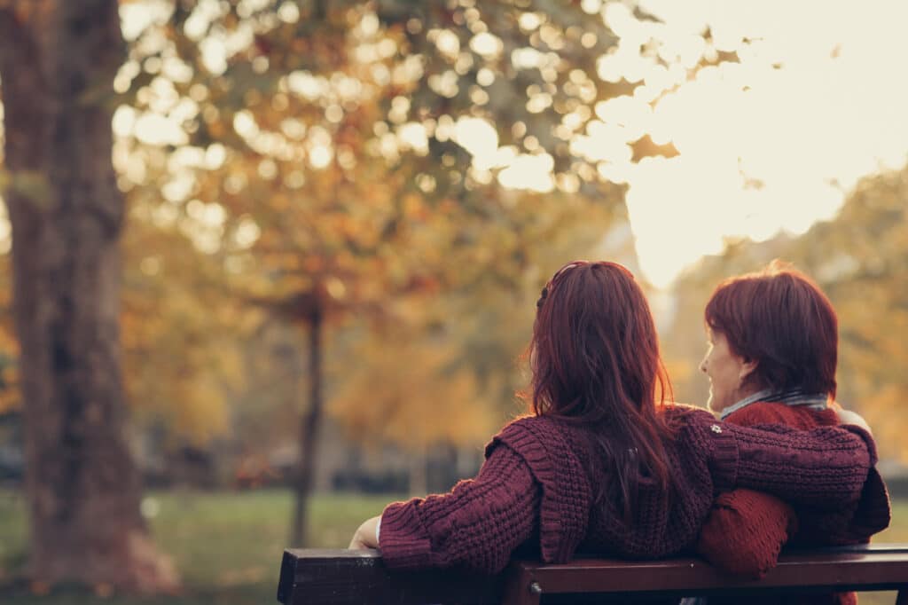 Mother and daughter sitting on park bench and enjoying sunny autumn day